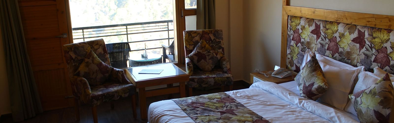 A cosy room with a large bed, floral-patterned bedding, and a seating area by the window at Dagshai Manor Kasauli - Inde Hotels.