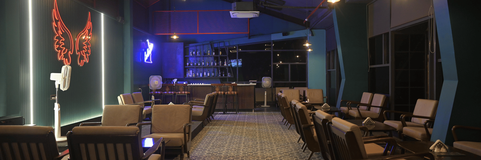 A wide evening view of the lounge bar with warm seating, patterned flooring, and soft neon lighting at Hotel Sonar Bangla Mayapur.