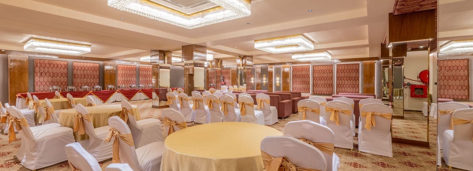 Round tables with yellow tablecloths and white chairs arranged under a decorative ceiling light at Hotel Highway King, Jaipur.