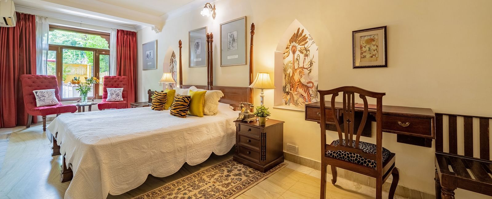 A bedroom with a four-poster bed, white linens, yellow cushions, a wooden desk, and a decorative niche in the wall | Dera Rawatsar, Jaipur