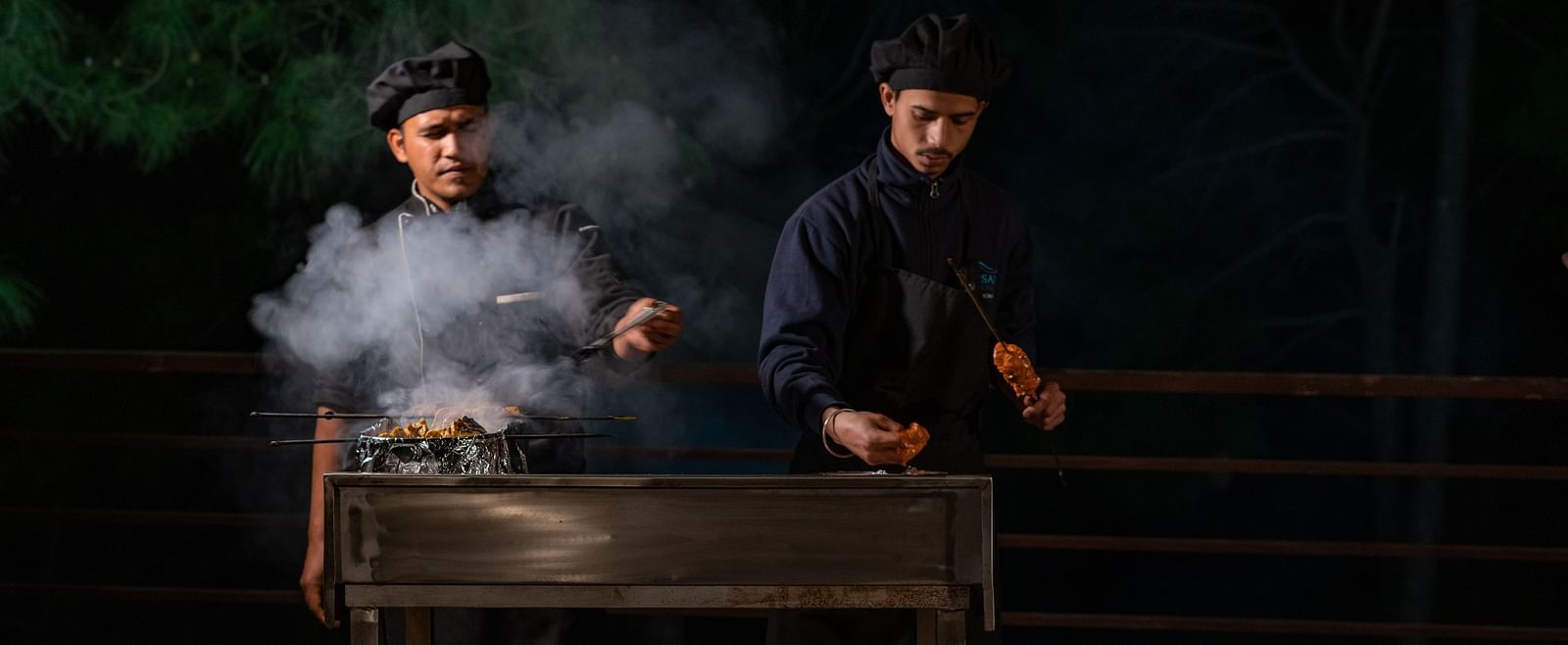 Two chefs preparing barbecues with smoke rising from the sizzling grills at BluSalzz Escapade Resort, Lansdowne
