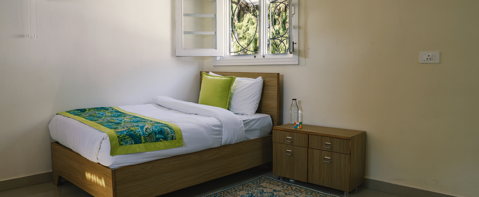 A spacious room with a single bed near the open window and a bedside table at BluSalzz Villas - The Green Roof, Bhimtal.