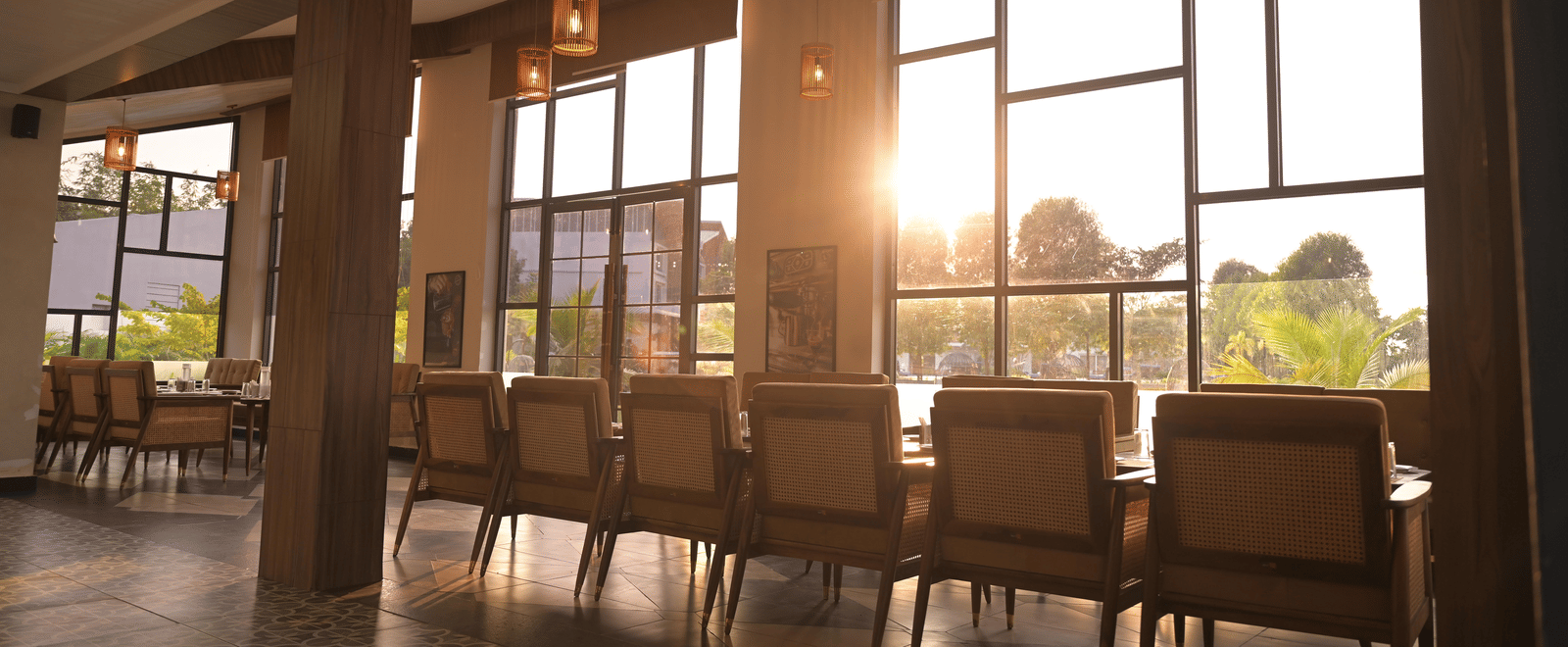 Indoor dining area with warm lighting and a sunset streaming through large windows at Hotel Sonar Bangla Mayapur.