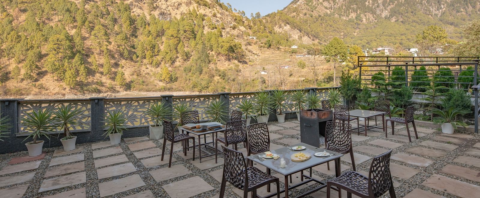 Outdoor dining tables set on a narrow balcony with views of green hills and a clear sky.