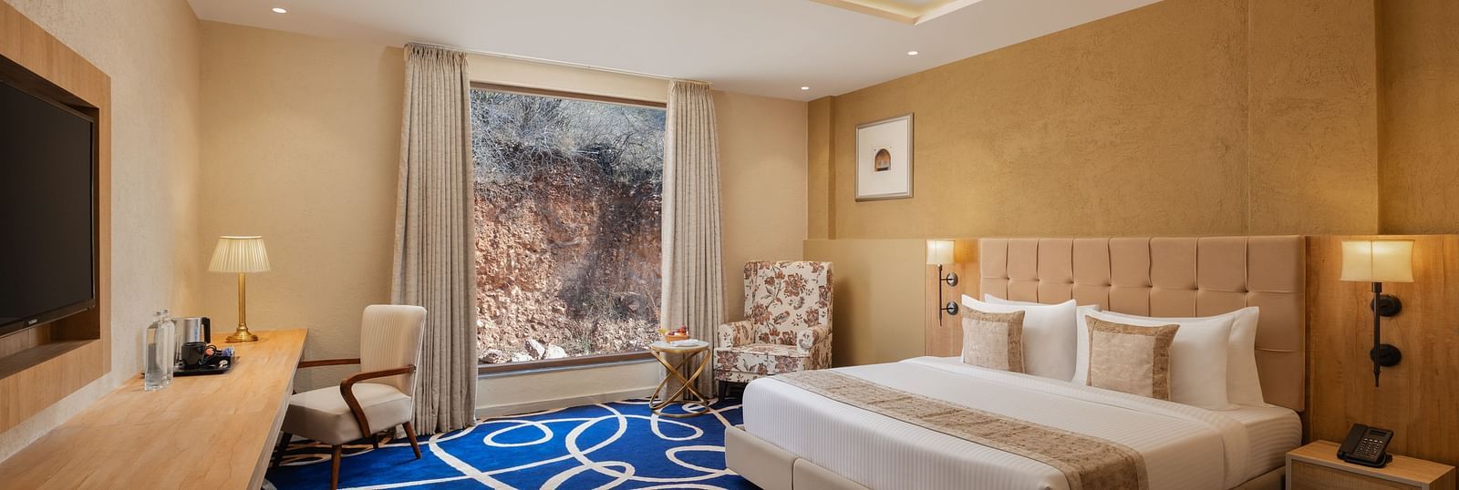 Deluxe room with a king size bed placed in front of a TV at Essentia Luxury Resort & Spa, Udaipur.