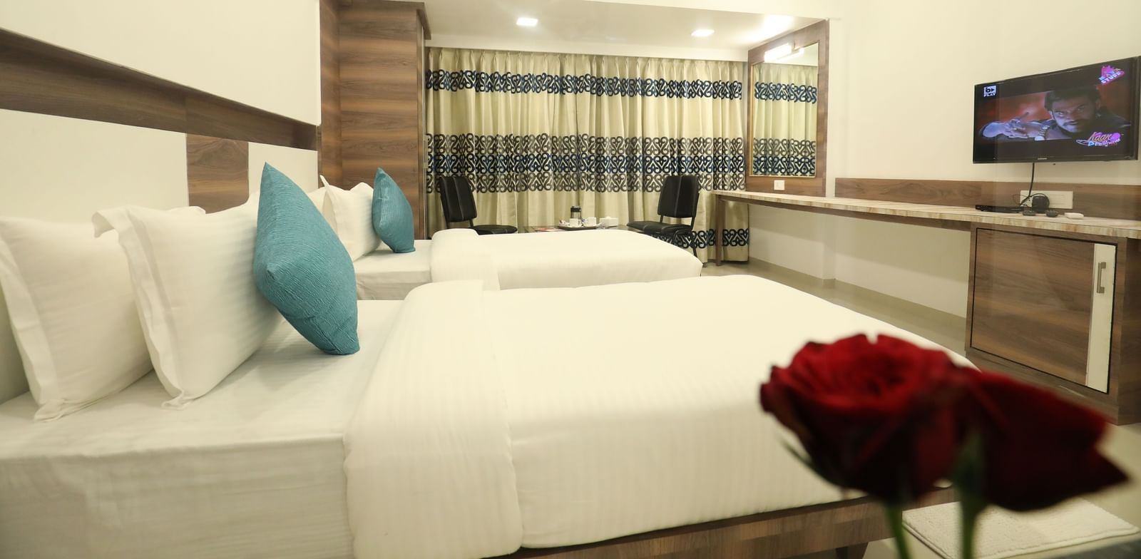A close-up view of a bed at Imperial Grande with white bedding and a red rose placed near it.
