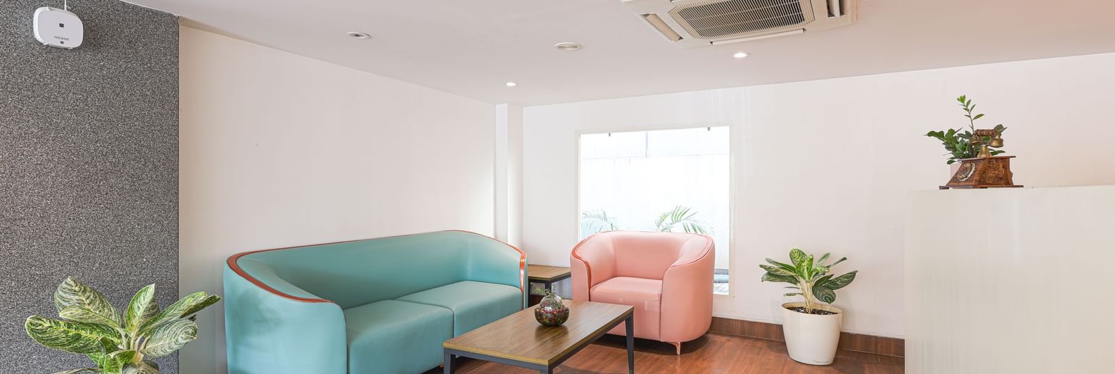 A modern and clean lobby area at Destino by Monday Hotels, Gachibowli, with a blue sofa and a pink armchair.