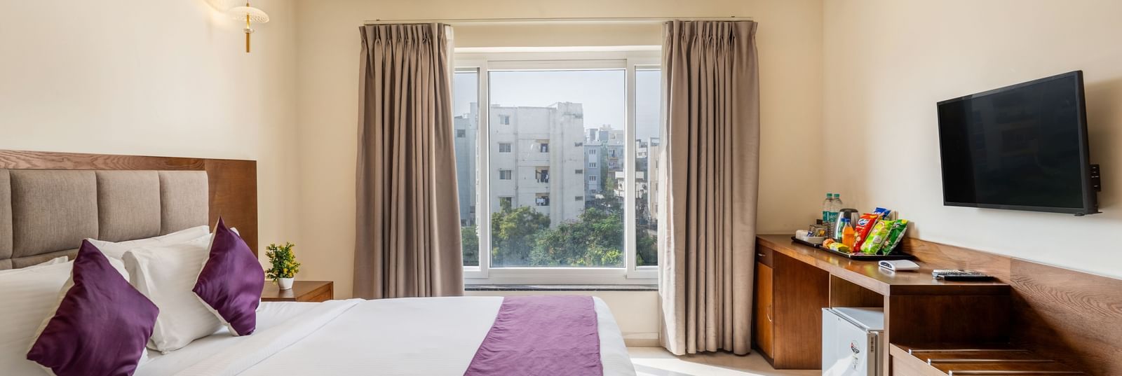 A well-lit room at Destino by Monday Hotels, Gachibowli, featuring a neatly made double bed, a wall-mounted TV, and wooden furnishings.