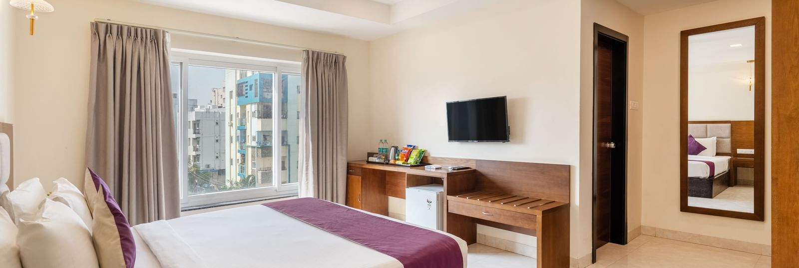 A spacious and well-lit room at Destino by Monday Hotels, Gachibowli, featuring a neatly made bed, a television, and a small round table with a fruit bowl.
