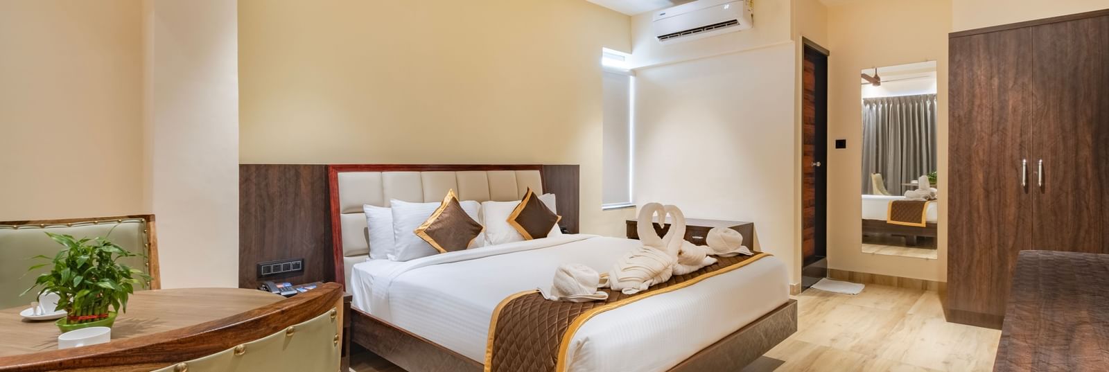 Spacious room at Monday Hotels Amalapuram Heights with double bed, ceiling fan, mirror, and air-conditioning.