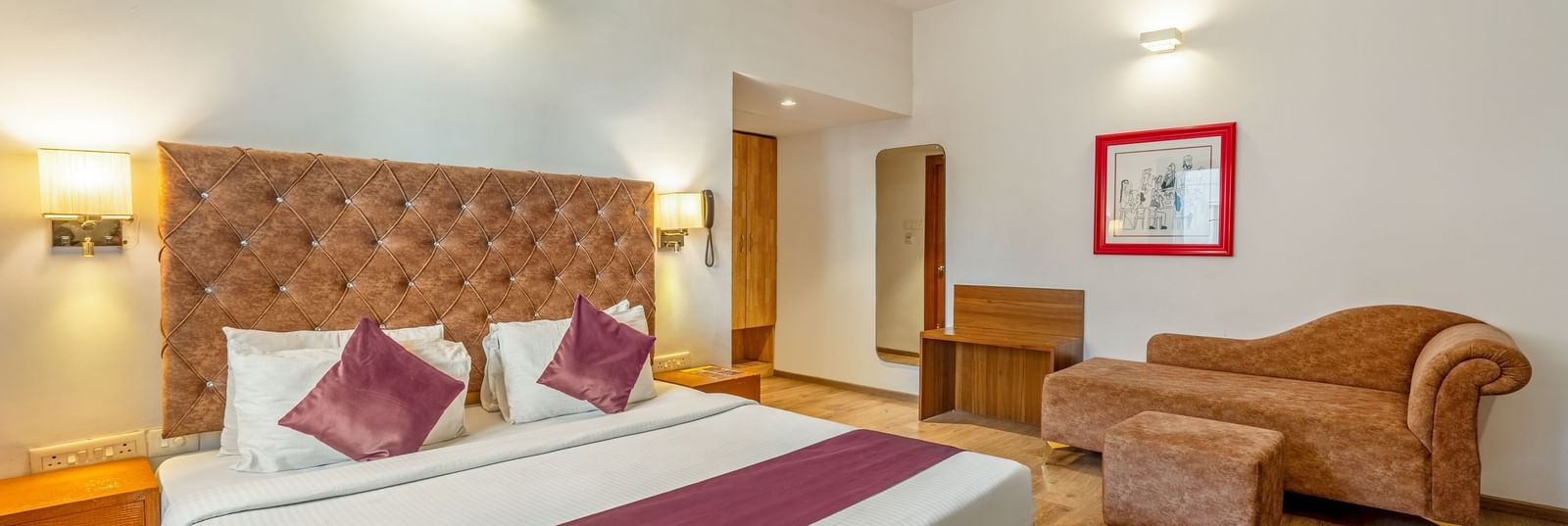A hotel room with a double bed, a cushioned sofa, and a wooden desk placed beside the bed - Monday Hotels HITEC City, Hyderabad