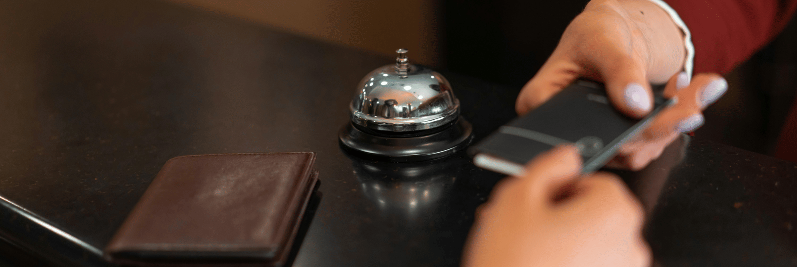 A hotel employee hands a black room key card to a customer across a dark reception desk with a bell.