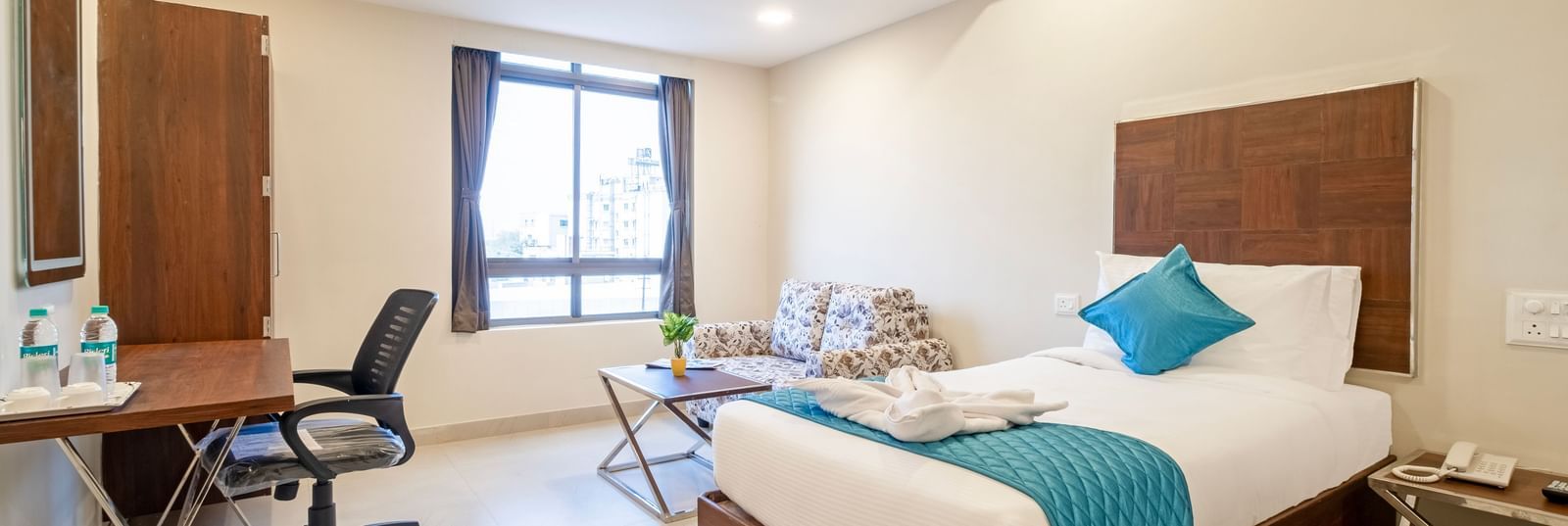 Modern room with king size beds work desk chair mirror and large window offering natural light at Swarna's The Capital.