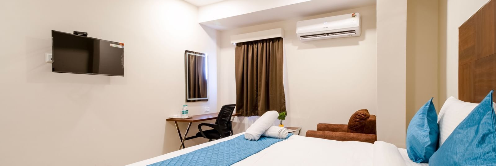 Bright bedroom with large bed blue accents television work desk seating area and air-conditioning for comfort at Swarna's The Capital.
