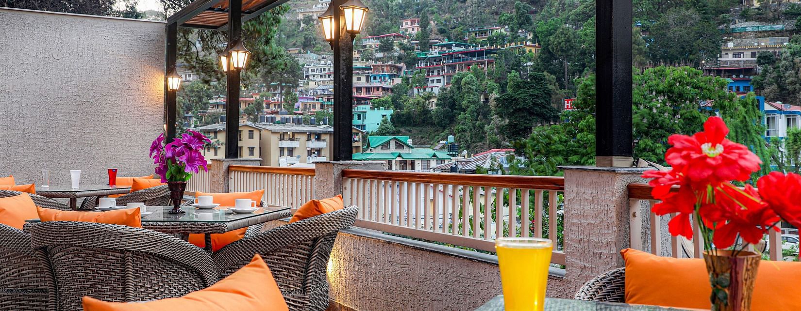 A rooftop cafe with lanterns, vibrant pillows, chairs and tables, all overlooking a scenic mountain view -  Vinsober Monal, Nainital