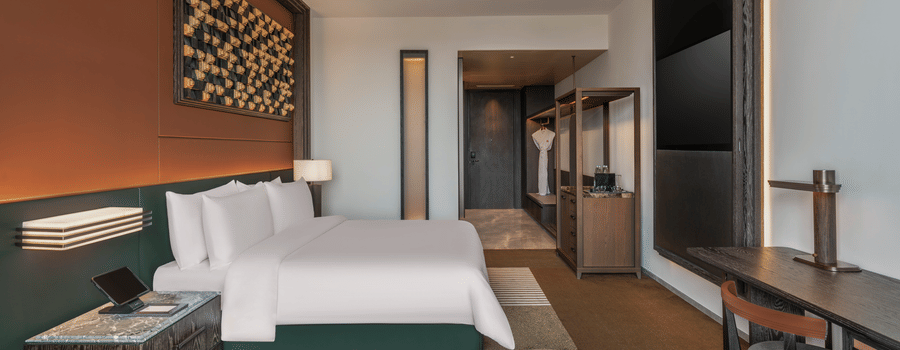 Side view of the Premium King room at The Residency Signature Madurai with a king bed, wall-mounted TV, wooden panelling, and warm ambient lighting.