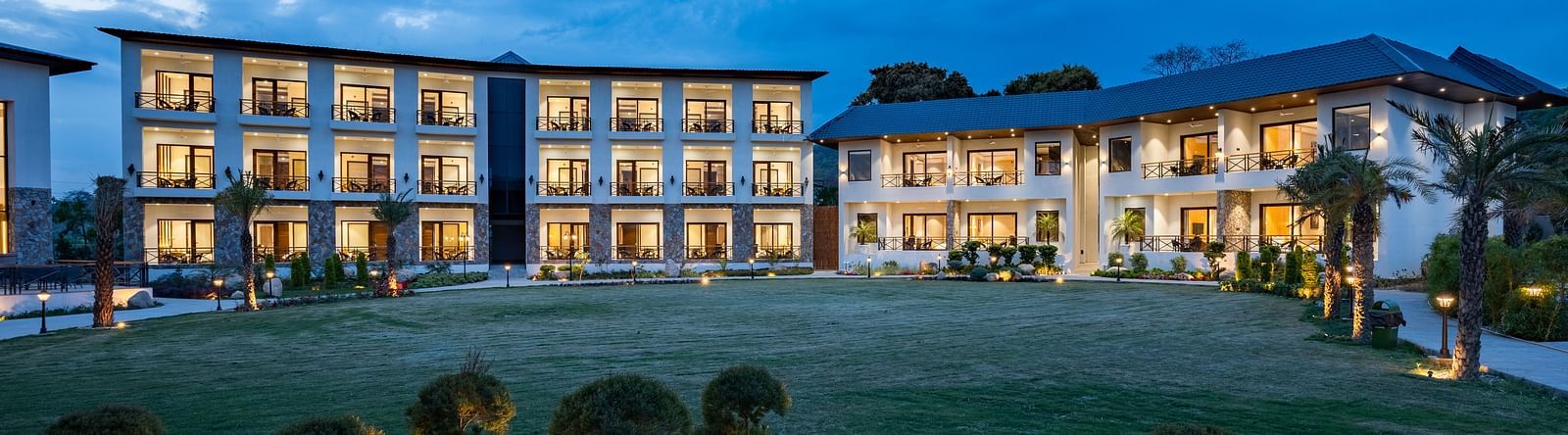 Exterior view of a well-lit hotel with spacious balconies and landscaped grounds at dusk - Shervani Hotels