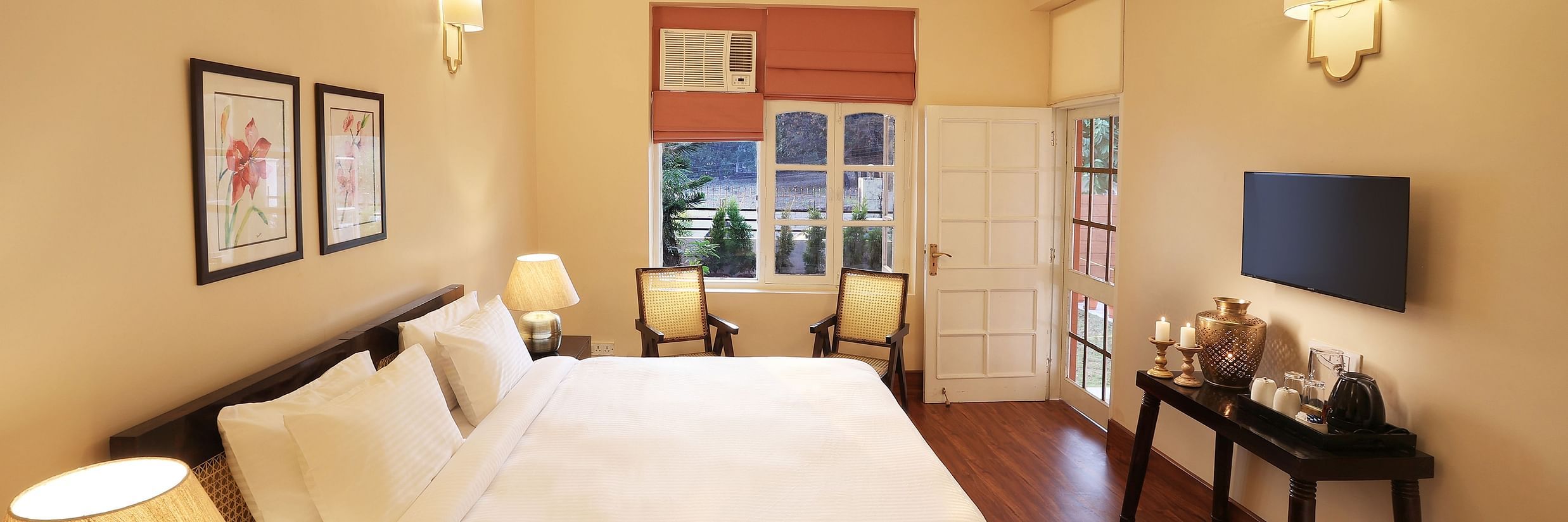 An image of a Super Deluxe Room equipped with soft bedding, modern furniture, flat TV screen, and a seating area with chairs  - Lamrin Boutique Cottages Rishikesh