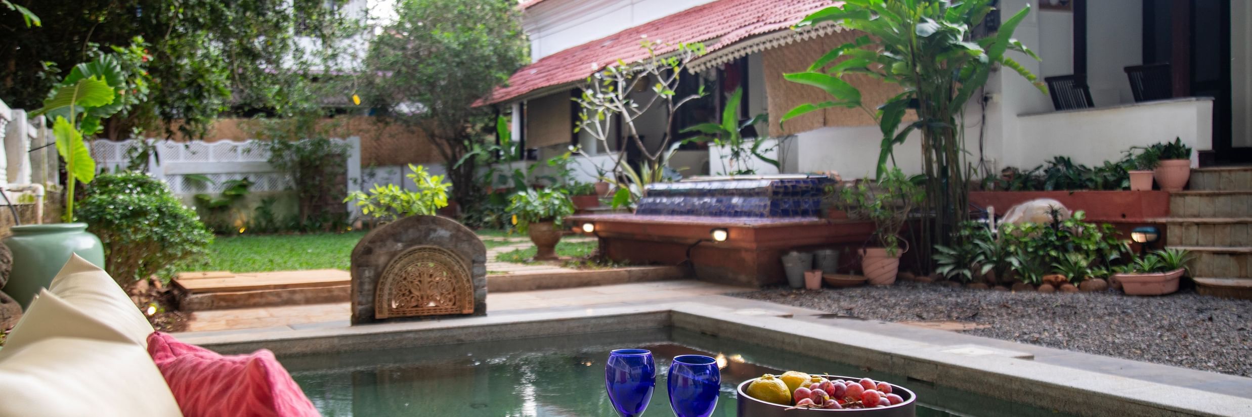 L shaped pool side with two blue wine glasses and surrounded by greenery @ Lamrin Ucassaim Hotel, Goa