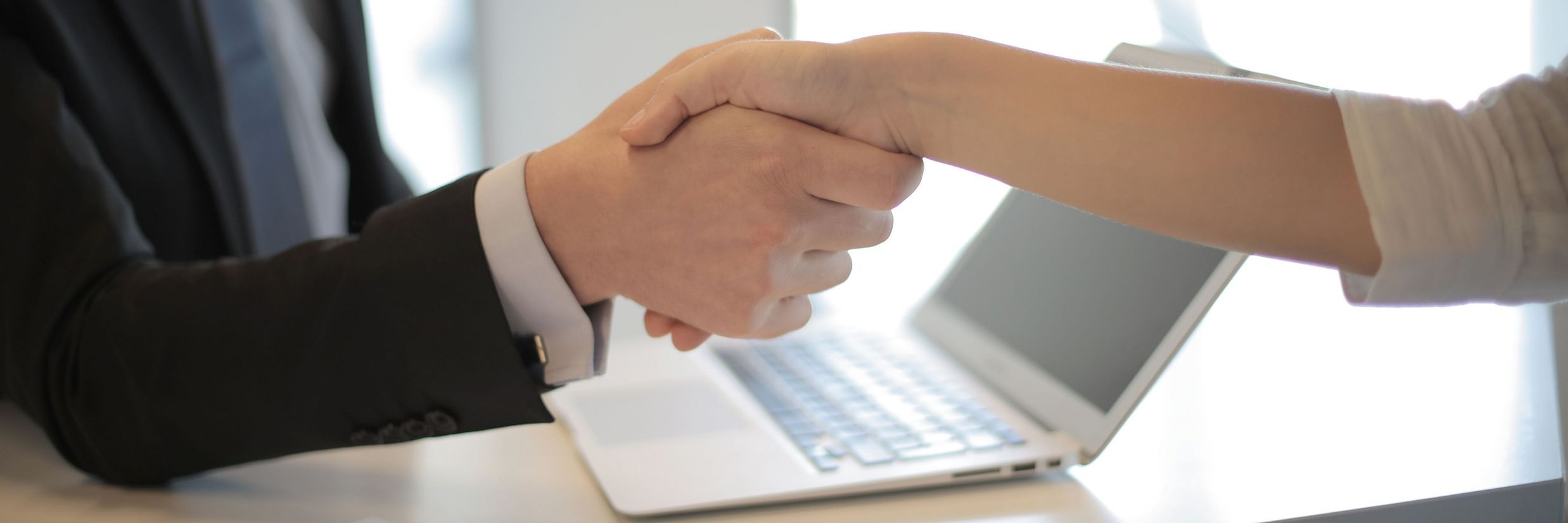 an image of two people shaking hands at an interview with a laptop kept on a table- goa job vacancy in hotel