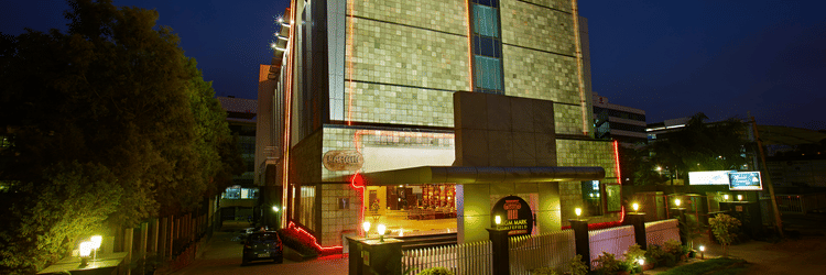 The MGM Mark Whitefield Business Hotel in Bengaluru glows warmly at night, a modern structure with red accents and inviting lights.