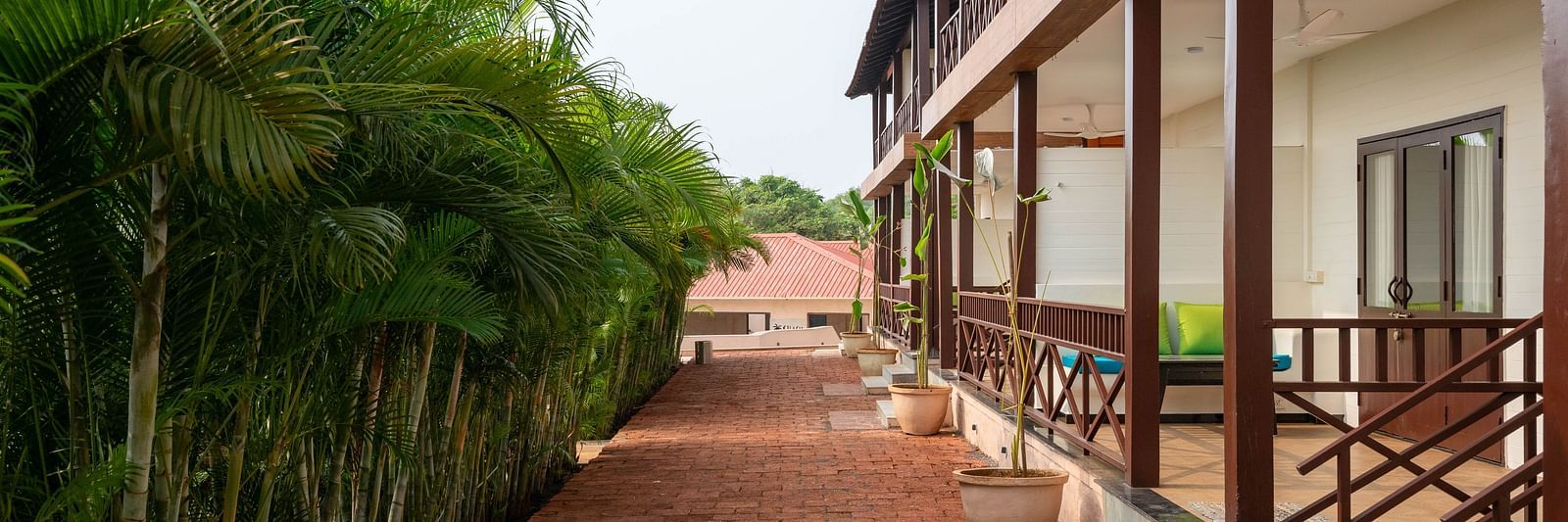 A clay-tiled pathway with a building on the right-hand side and small bamboo shoots lining the left-hand side - Crescent Resort, Goa.