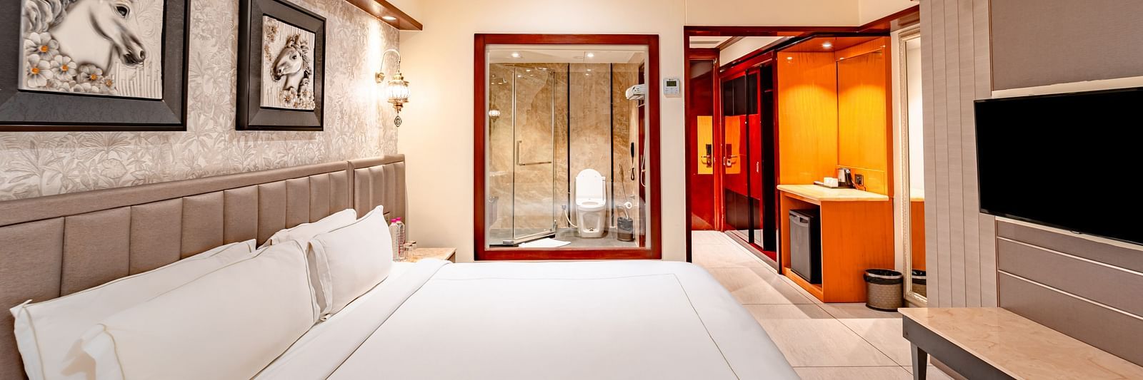 Deluxe Room side view features a spacious bed with a wall-mounted television directly opposite, two photo frames above the headboard at Crescent Spa & Resort, Indore