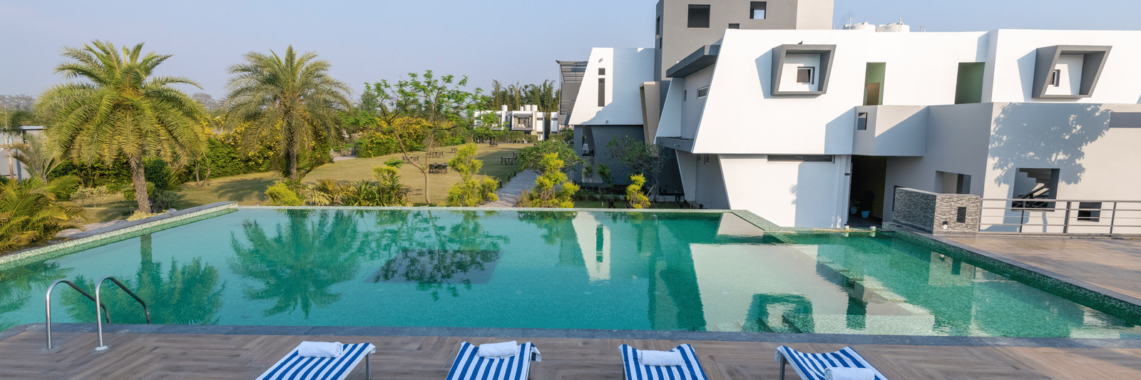 Pool area with lounge chairs placed beside it, offering a view of trees on one side at DLS Forest Vines Resort.
