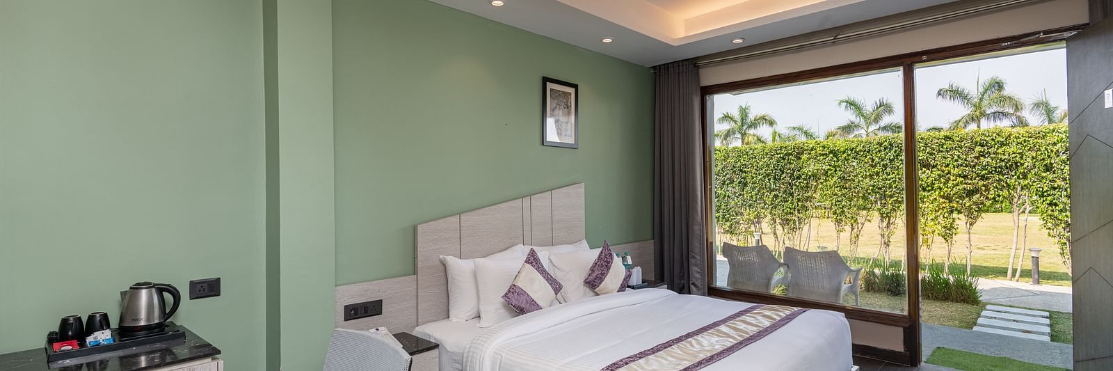 A spacious room at DLS Forest Vines Resort, complete with a large bed, bedside table, table and chairs, and a glass door opening to the balcony.