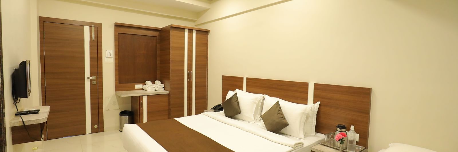 Extended view of the plush queen size bed in the Deluxe Room of the Highland Resort furnished with a wardrobe, wall-mounted TV, and bedside tables.