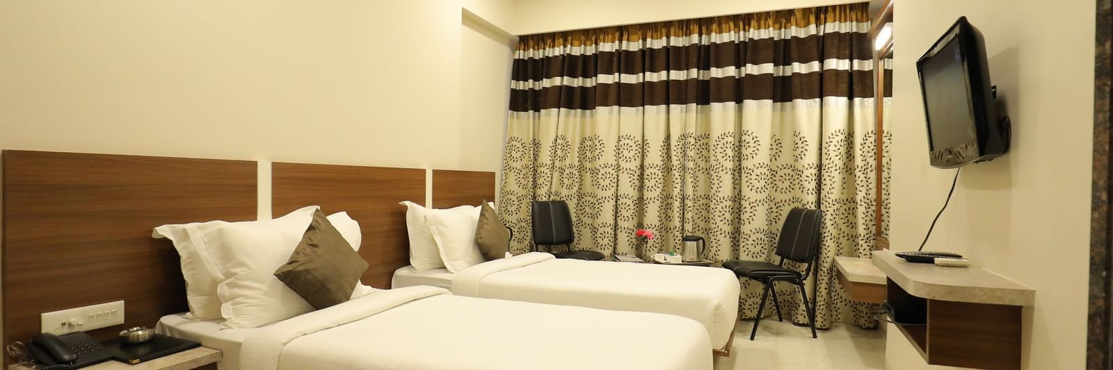 A Super Deluxe Room of Highland Resort furnished with twin beds, a wall-mounted TV, seating area for two, and closed curtains.