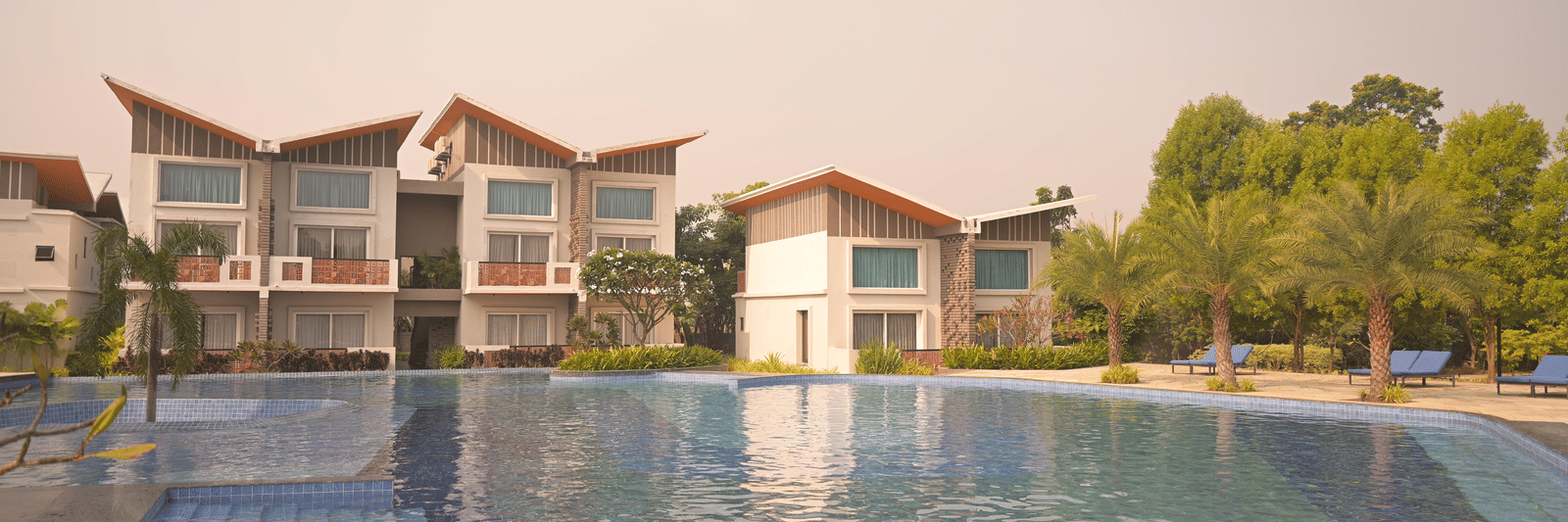 A swimming pool overlooking modern villa-style buildings surrounded by greenery at Hotel Sonar Bangla Mayapur.