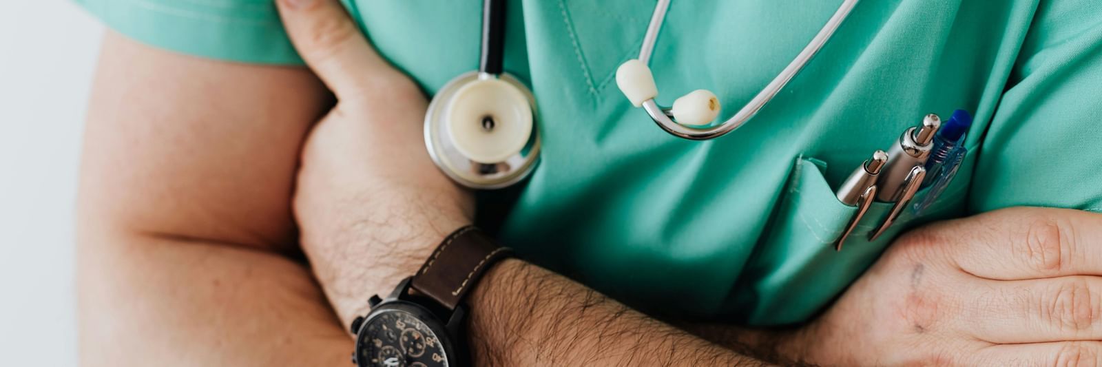 A person in green scrubs with a stethoscope around their neck, standing with their arms crossed.