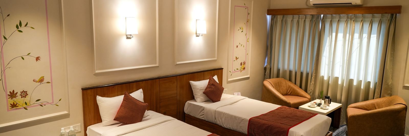 Comfortable twin room with two neatly arranged beds and cosy seating at Pravasa Hotel Kolhapur.
