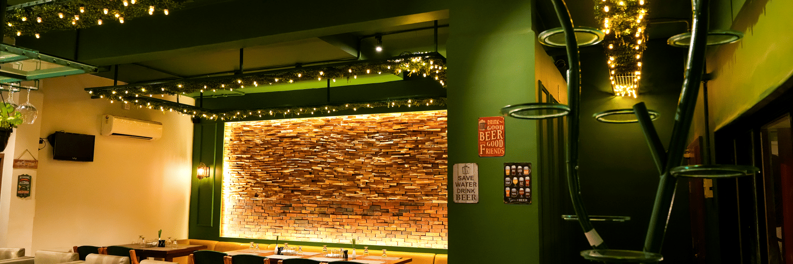 A vibrant lounge area with striking green walls, comfy seating, and a feature wall of exposed brick at Pravasa Hotel, Kolhapur.