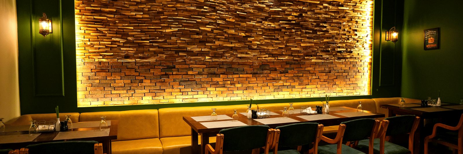  A warm dining section with a long yellow upholstered booth and a dramatic backlit stone feature wall at Pravasa Hotel, Kolhapur.
