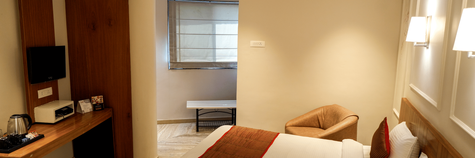  A well-equipped guest room with a wooden desk, a kettle, and a separate sitting area near a window at Pravasa Hotel, Kolhapur. 