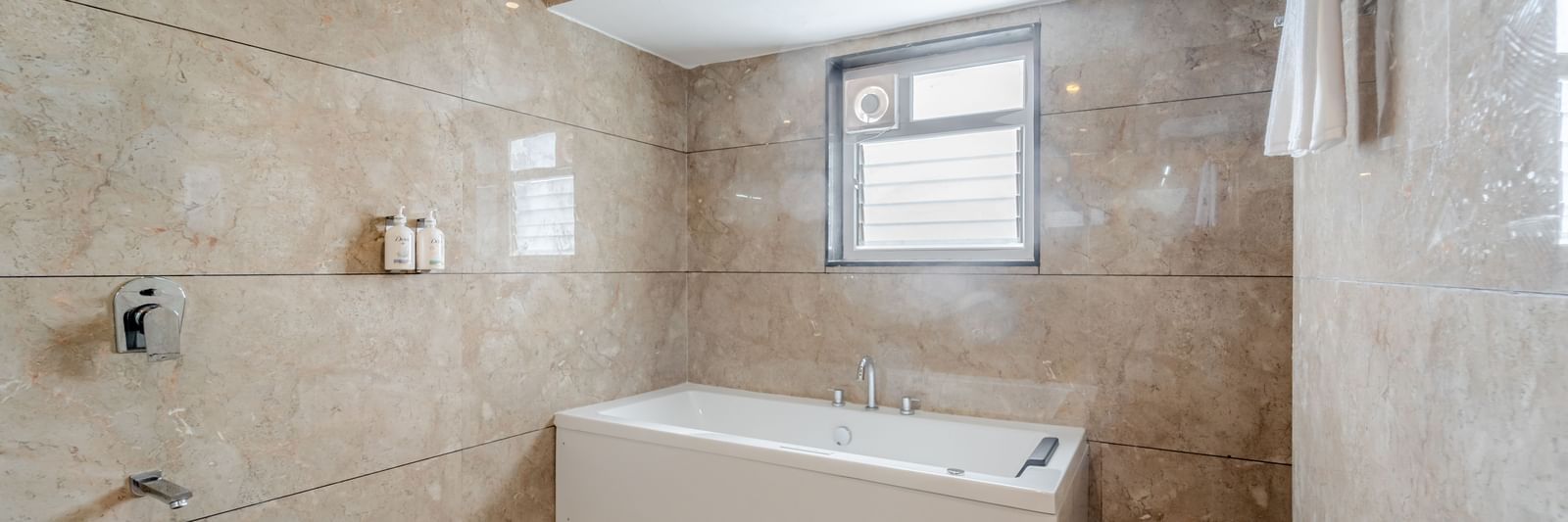 A suite bathroom with a white bathtub and patterned beige tiles | Suite | Pravasa Hotel, Vijayapura