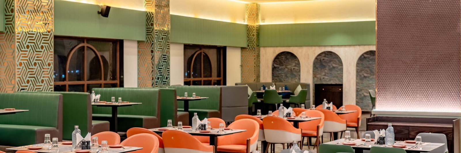Dining area with green and orange chairs and decorative hanging elements | Pravasa Hotel, Vijayapura