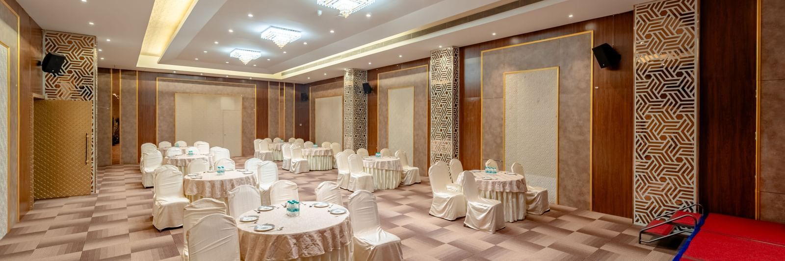 Event hall configured with round tables and draped chairs for a banquet | Meetings & Events | Pravasa Hotel, Vijayapura
