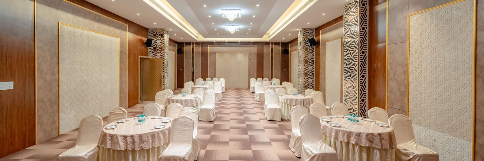 A conference room with round tables and beige chairs, ready for an event | Meetings & Events | Pravasa Hotel, Vijayapura