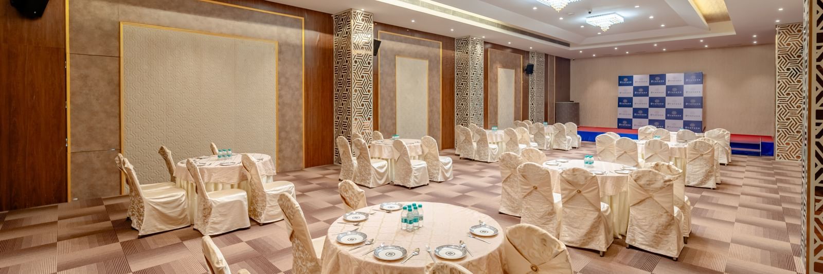 A banquet hall with round tables and beige chairs | Meetings & Events | Pravasa Hotel, Vijayapura