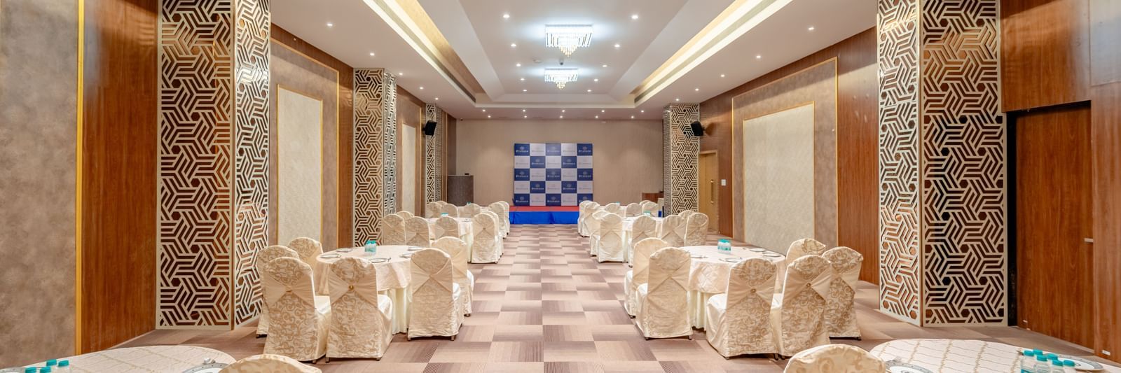 Meeting room with multiple rows of chairs facing a stage area | Meetings & Events | Pravasa Hotel, Vijayapura