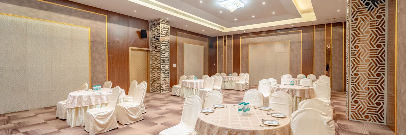 Spacious banquet hall with round tables and elegant chair covers | Meetings & Events | Pravasa Hotel, Vijayapura
