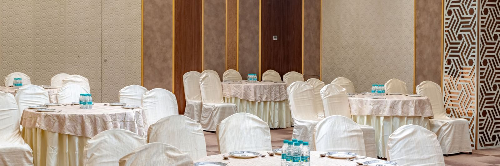 A banquet hall with round tables and elegant chairs | Meetings & Events | Pravasa Hotel, Vijayapura