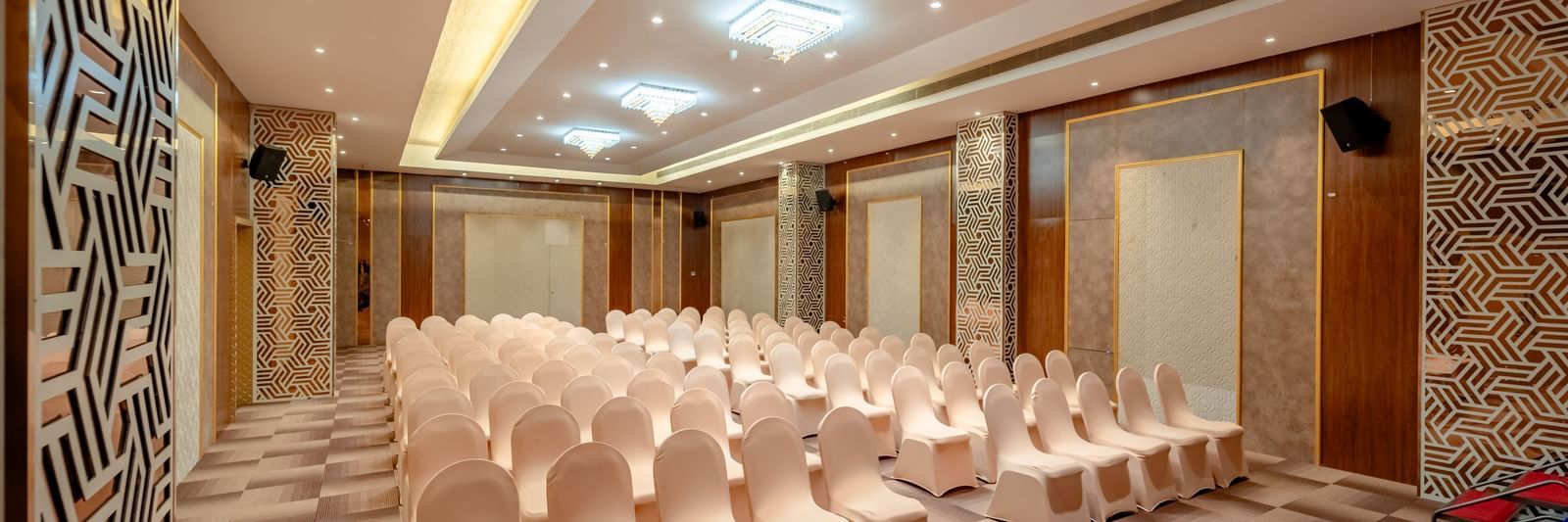 An empty ballroom set up with rows of beige chairs | Meetings & Events | Pravasa Hotel, Vijayapura