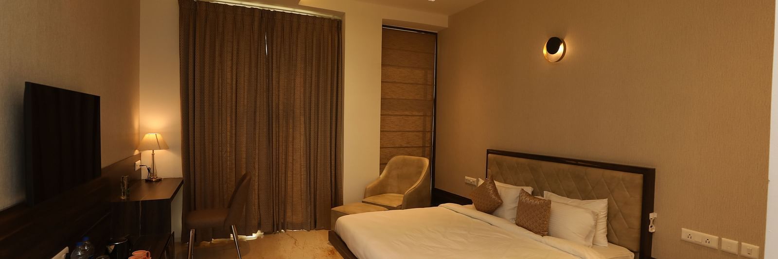 Hotel bedroom interiors with chairs television and a white king size bed - Welcome Inn Hotels