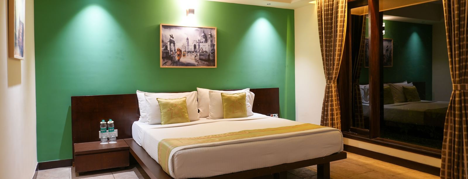 Bedroom in the Retreat Villa at Vedic Village Spa Resort with a double bed, wooden headrest, ceiling fan, and a large wall-to-wall window offering a night-time view of the outdoors.