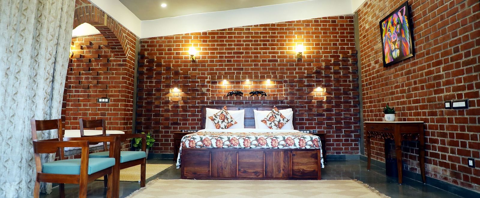 A bedroom at Tisya Farms, Gurgaon with a double bed, brick walls, ceiling fan, chairs, and patterned bed linens.