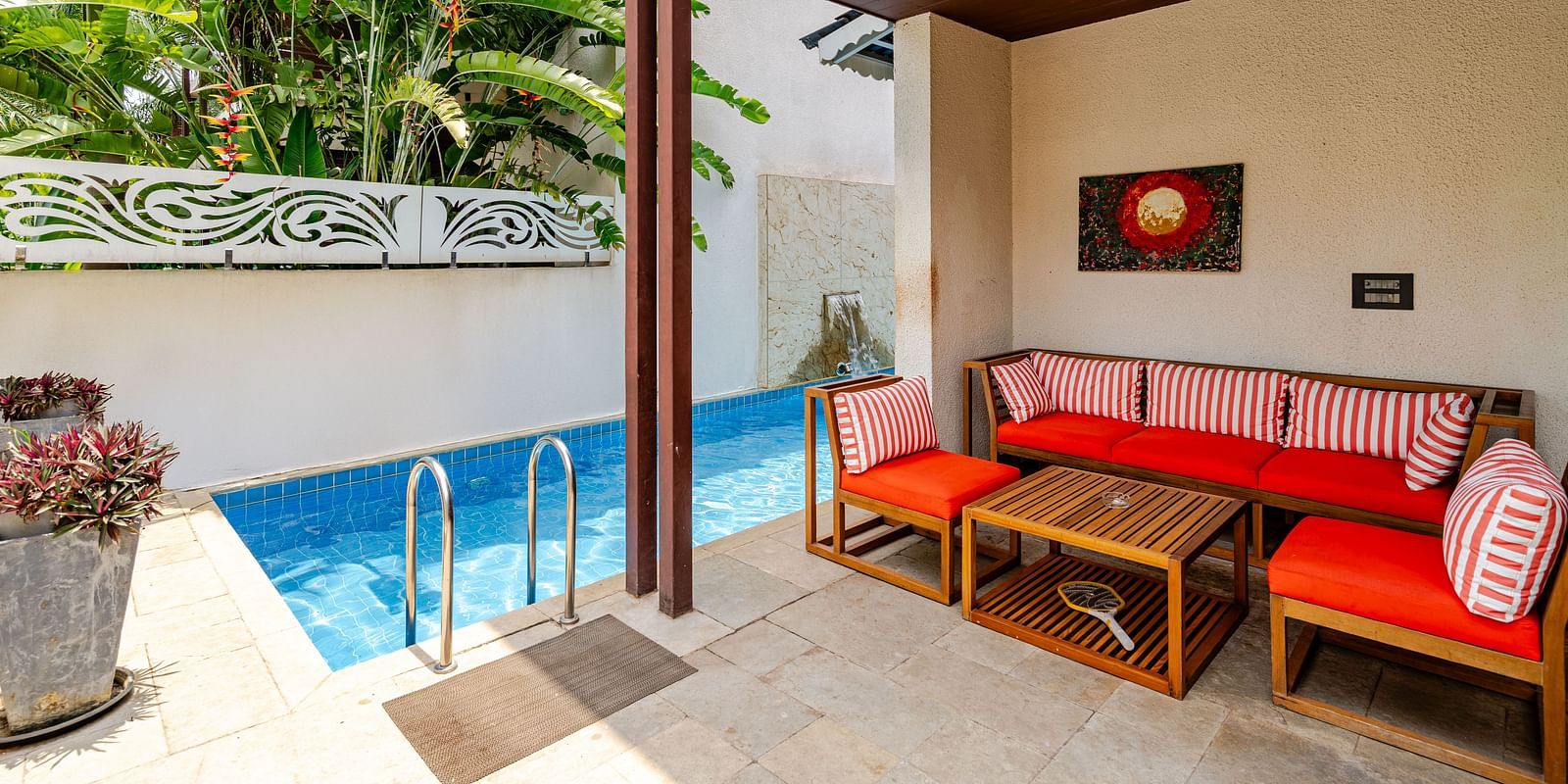 Private outdoor seating area at Lindsay Manor with red cushioned bench, wooden table, and view of the pool.
